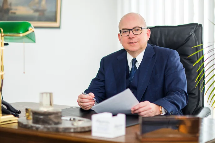 Foto von Dr. Andreas Domeyer sitzend am Schreibtisch mit einem Kugelschreiber in der rechten und einem Dokument in der linken Hand.